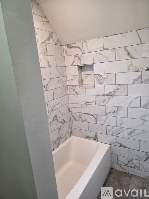 A white bathtub sits in a bathroom with marble tile walls.