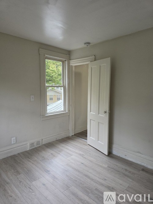 A room with a white door and a window with a view of a building across the street.