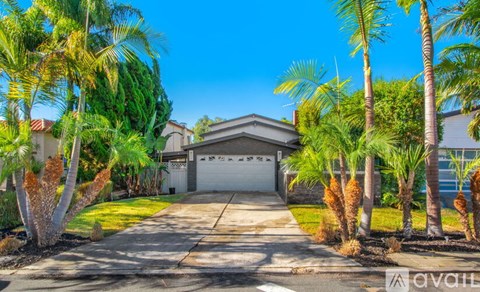 A house with a driveway and palm trees in front.