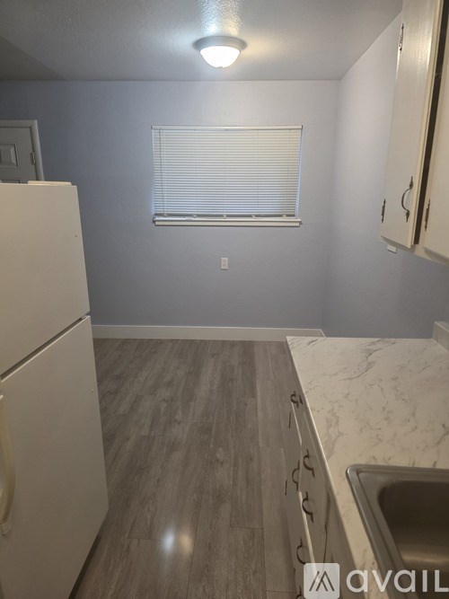A kitchen with a white refrigerator, wooden floor, and white cabinets.