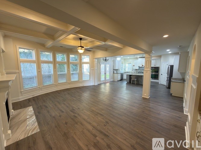 A spacious room with wooden floors and a fireplace on the left side.