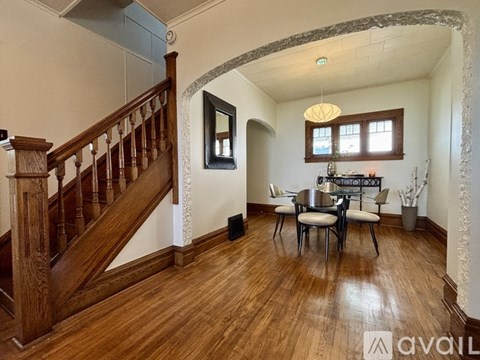 A living room with a wooden staircase and a dining table with chairs.
