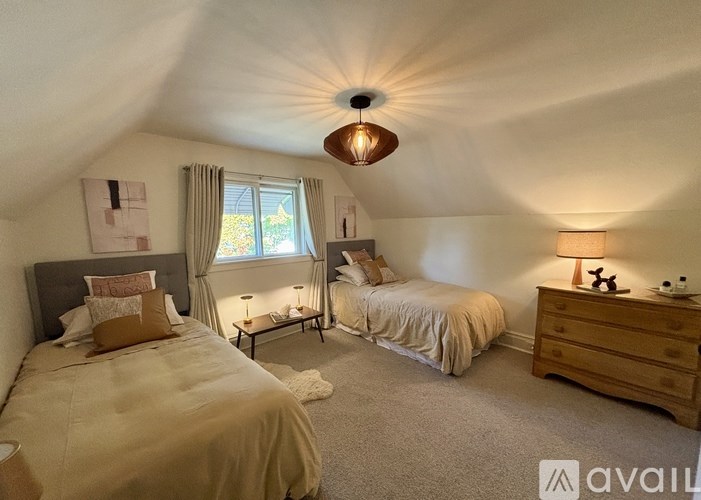 A bedroom with two beds, one with a white comforter and the other with a beige comforter, a wooden dresser, and a window with curtains.