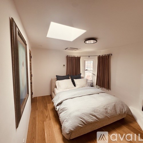 A bedroom with a bed, pillows, and a skylight.