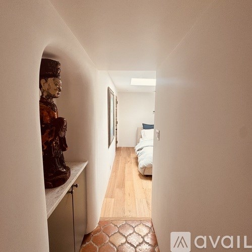 A hallway with a statue on the left and a bed on the right.