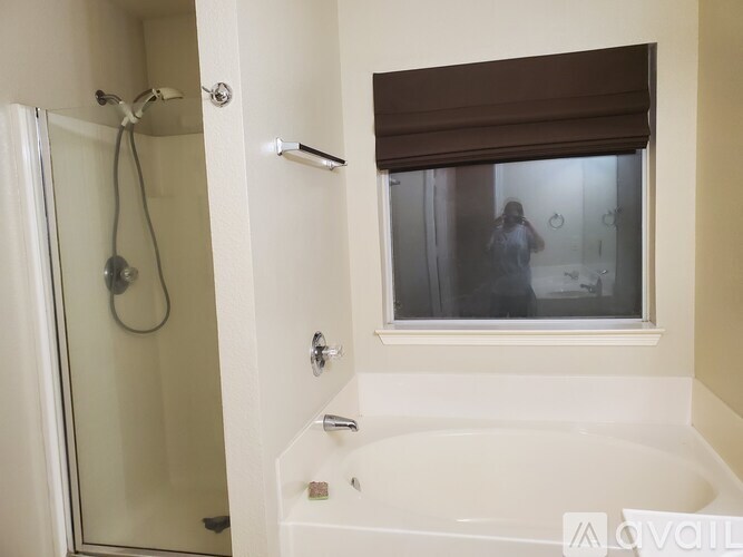 A bathroom with a white tub and a window with a brown blind.