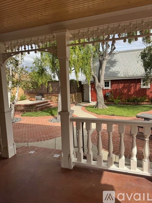 A patio with a white railing and a view of a backyard with a tree and a red building.