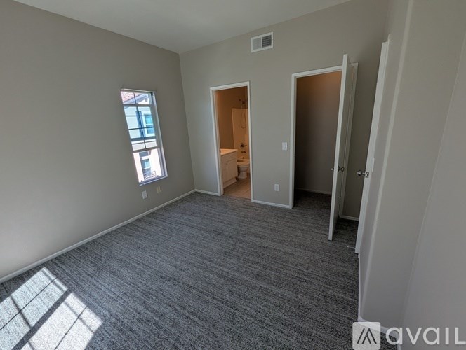A room with a grey carpet and a window on the left side.