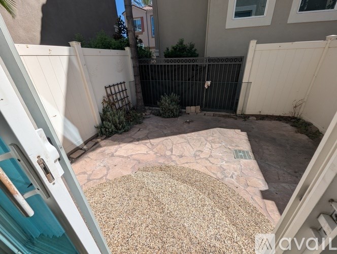 A backyard with a fence, a gate, and a rug on the ground.