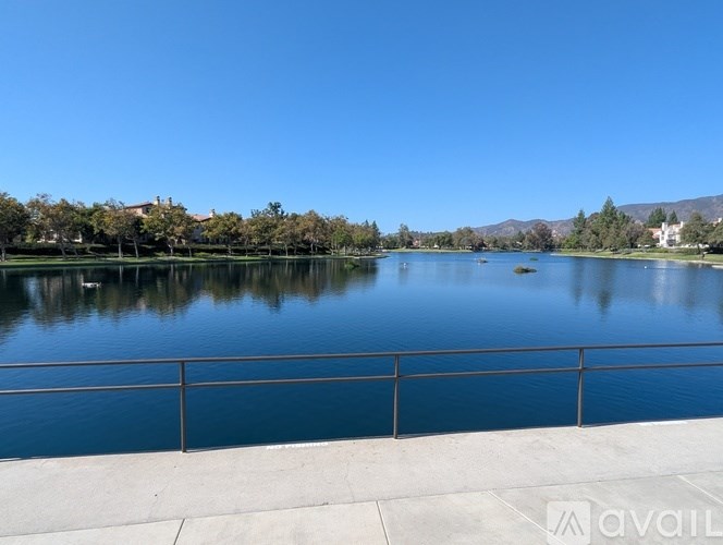 A serene lake with a clear blue sky and a metal railing in the foreground.