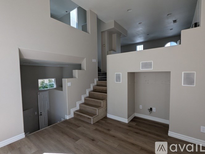 A spacious room with wooden floors and a staircase leading to another level.