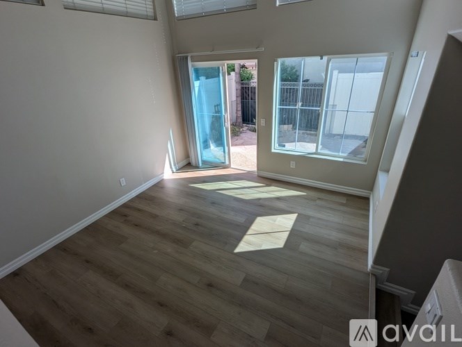 A room with wooden flooring and a large window with a view of a fence and trees.