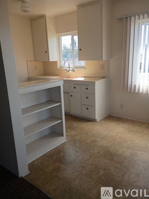A kitchen with white cabinets and a window with blinds.