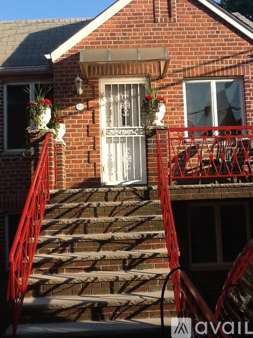 A red staircase leads up to a white door on a brick building.
