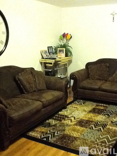 Two brown couches in a living room with a clock on the wall.