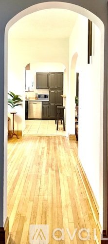 A hallway with wooden floors and a white archway leading to a kitchen.