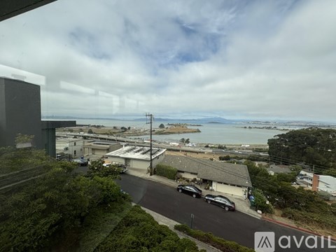 A car is parked on the side of a road with a view of the ocean in the distance.