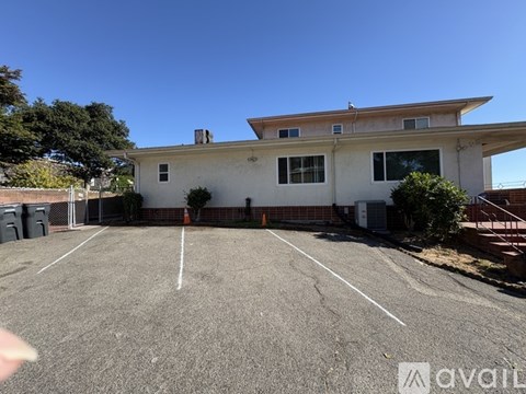 A large, empty parking lot in front of a two-story building with a white facade and a red brick base.