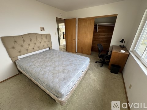 A bedroom with a large bed, a desk with a chair, and a window with blinds.