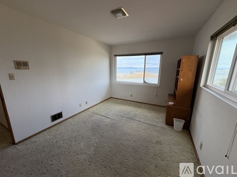 A room with a carpeted floor, a window with a view of the ocean, and a wooden cabinet.
