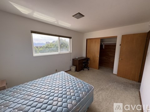A bedroom with a large bed and a desk with a window overlooking the outdoors.