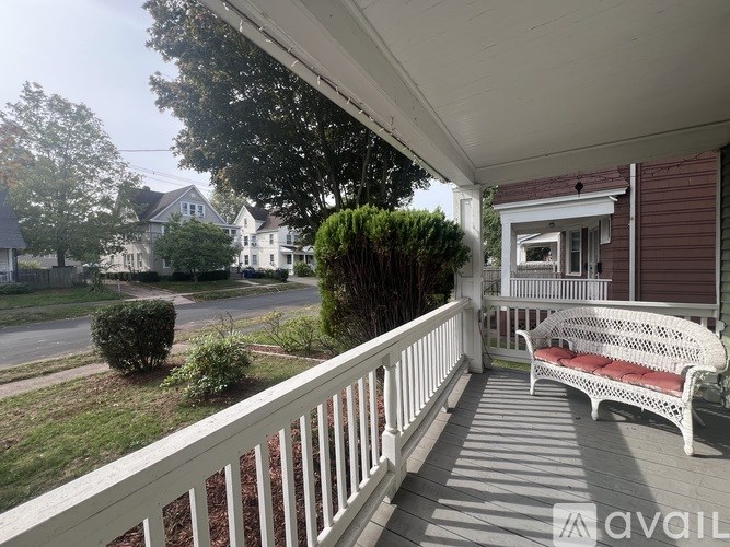 A white bench with a red cushion is on a porch.