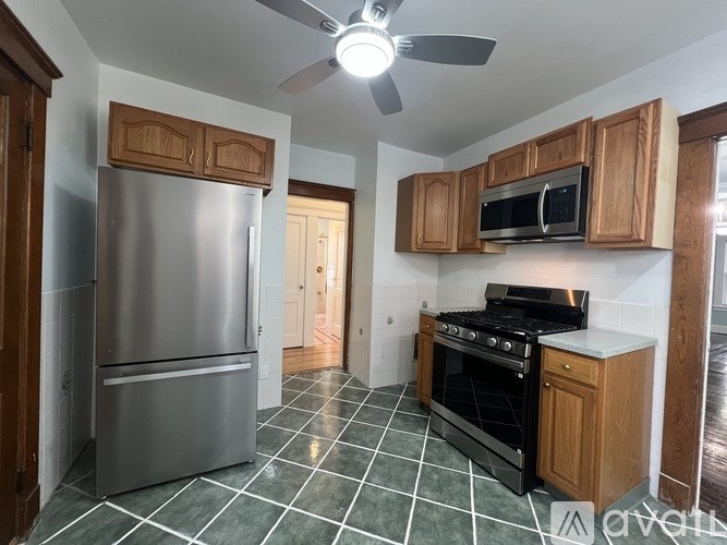 A kitchen with a stainless steel refrigerator, black stove, and wooden cabinets.