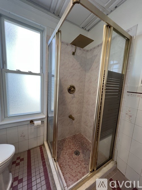 A bathroom with a toilet, a window, and a shower with a glass door.