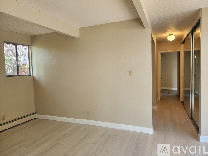 A spacious room with wooden flooring and a window on the left side.