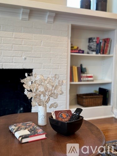 A vase with flowers sits on a table next to a book and a remote.