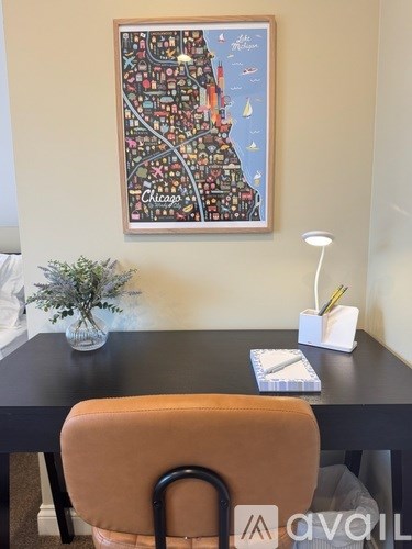 A framed map of Chicago is hanging on the wall above a desk with a chair and a lamp.