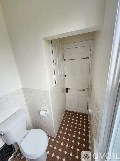 A white toilet in a small bathroom with a brown and white tiled floor.
