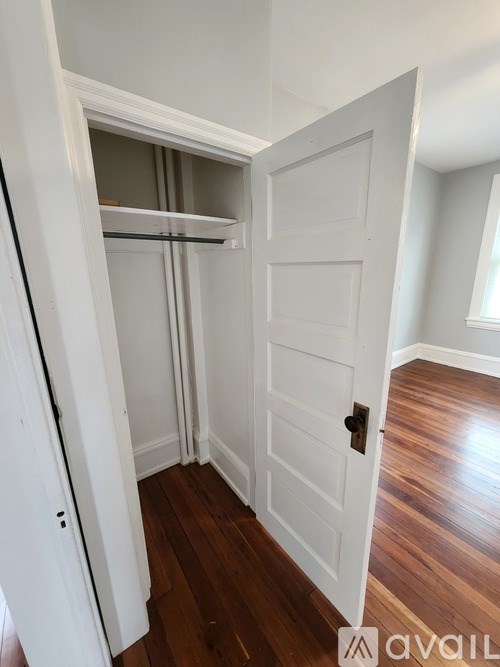 A white door is open to a room with wood flooring.