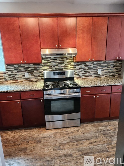 A kitchen with red cabinets and a stone backsplash.