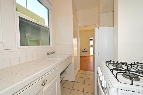A white kitchen with a gas stove and a window.