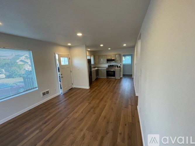 A spacious room with wooden flooring and a kitchen area in the background.