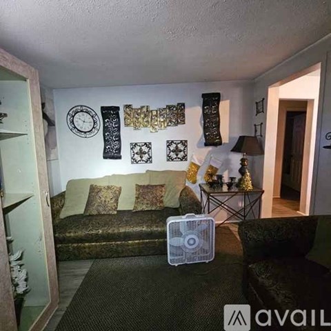 A living room with a couch, a fan, and a table with a lamp.