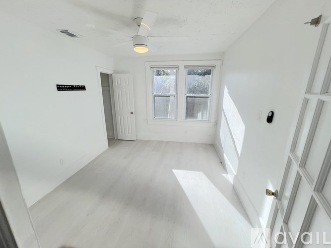 A spacious room with white walls and a large window overlooking greenery.