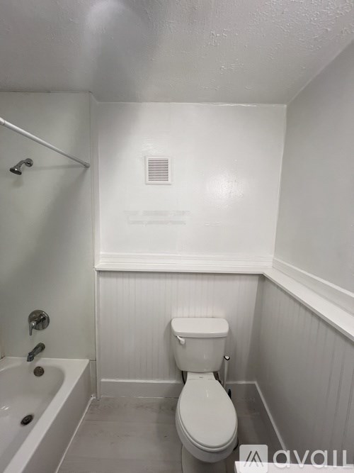 A white toilet in a small bathroom with a white tub and a white shower head.