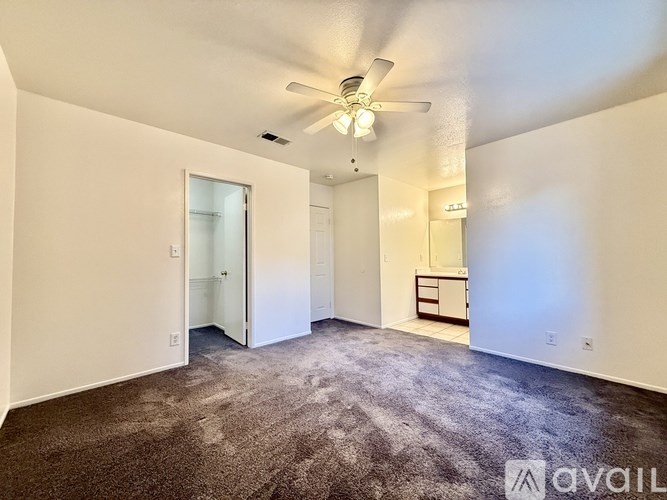 A carpeted room with a ceiling fan and a door leading to another room.