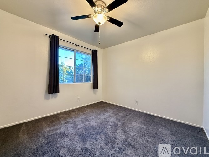 A room with a ceiling fan and a window with blue curtains.