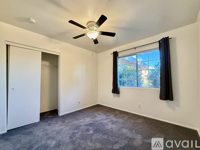 A room with a ceiling fan and a window with black curtains.