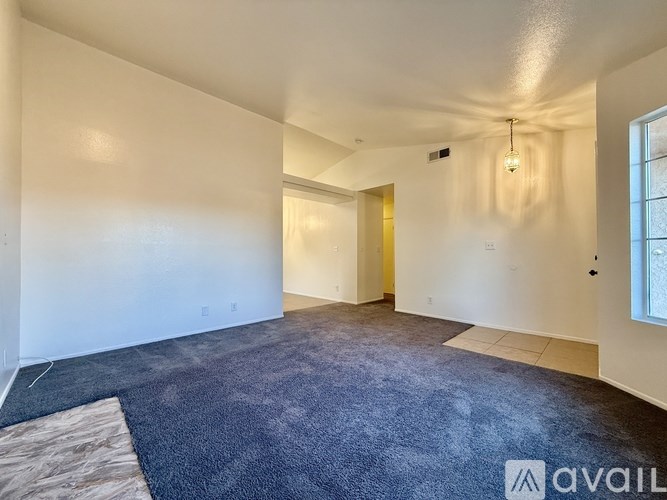 A spacious room with a carpeted floor and a window on the right side.