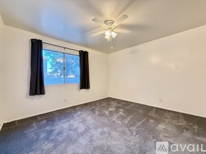 A room with a ceiling fan and a window with black curtains.