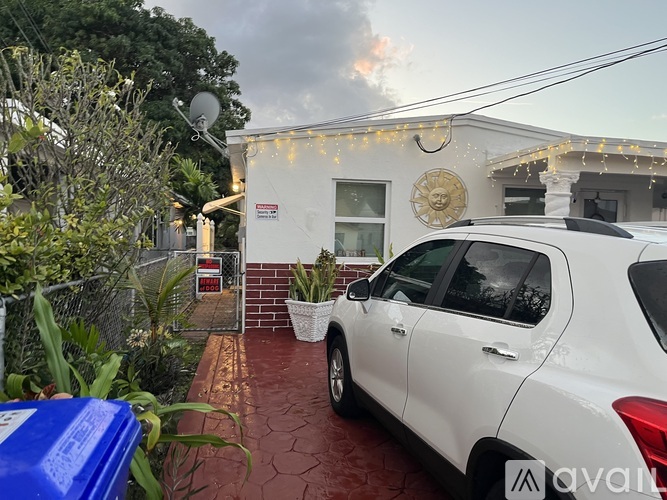 A white car is parked in front of a house with a red brick walkway.