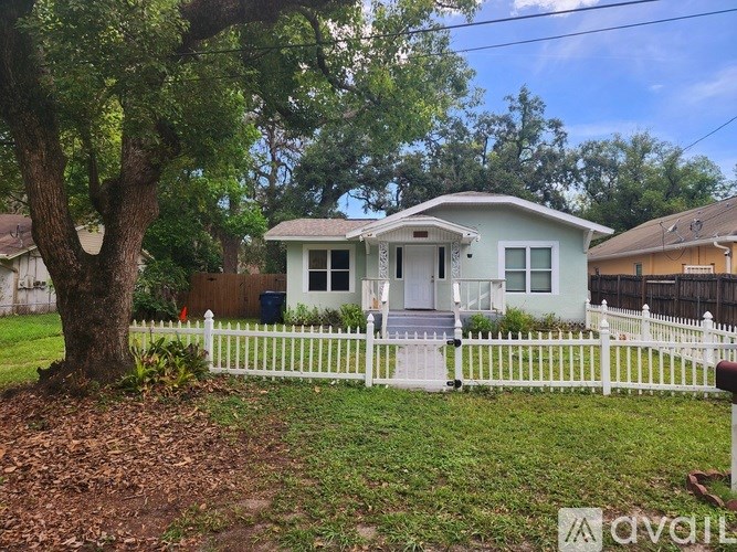 A white picket fence surrounds a two-story house with a front porch.