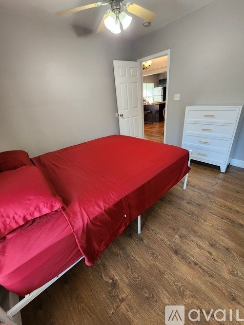 A bed with a red cover is in a room with a ceiling fan.