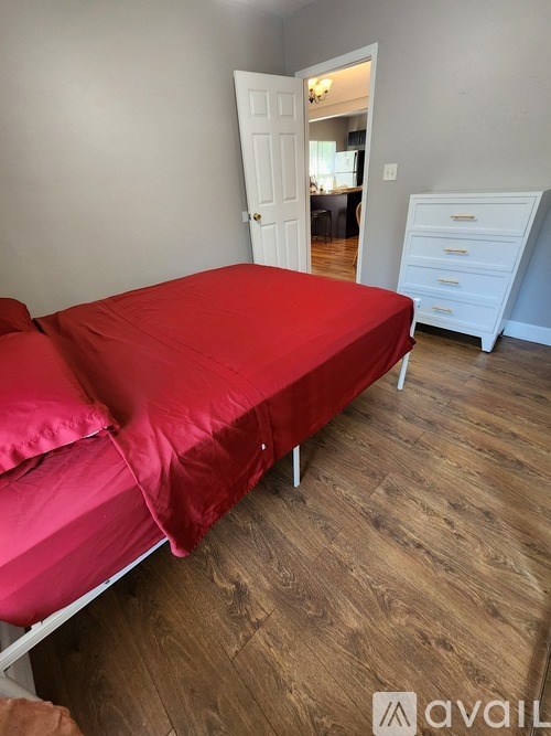 A bed with a red cover is in a room with wooden flooring.