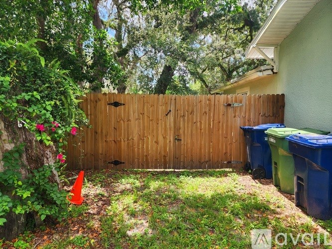 A backyard with a wooden fence, a green trash bin, and a red cone.