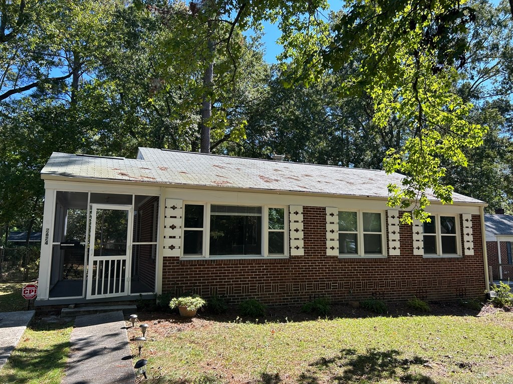 A small house with a porch and a tree in front.